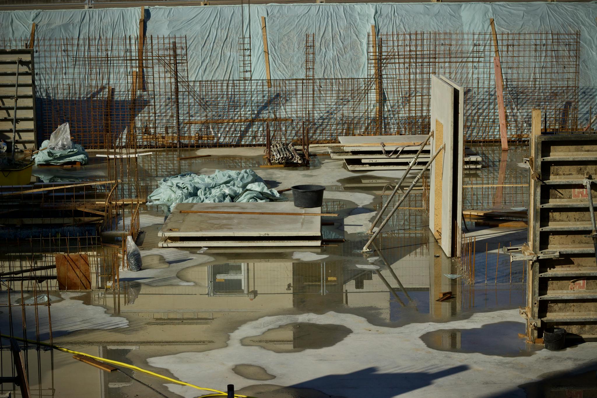 A flooded construction site with scattered materials and visible metal reinforcement.